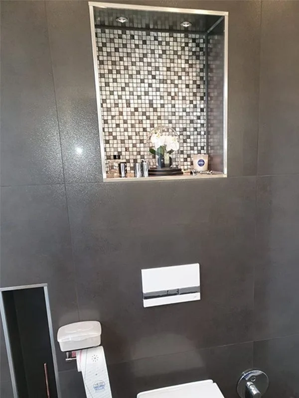 Bad mit dunklen Großformatfliesen, beleuchteter Mosaik-Nische und Drückerplatte