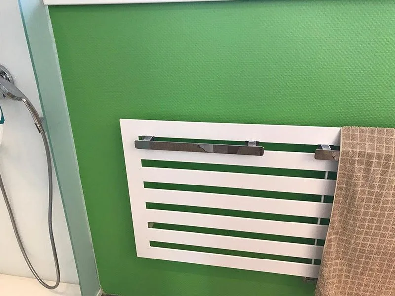 Weißer Design-Handtuchheizkörper vor einer grünen Wand